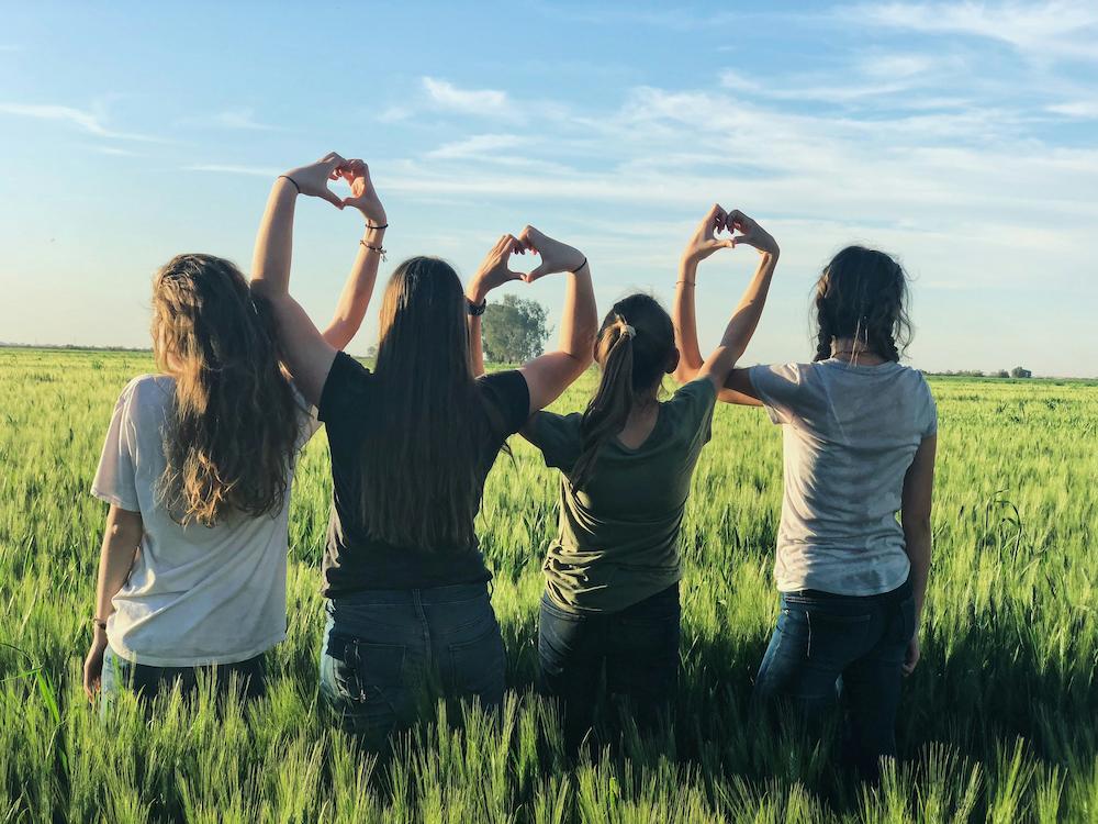 Girls standing together in a field making love hearts with their arms